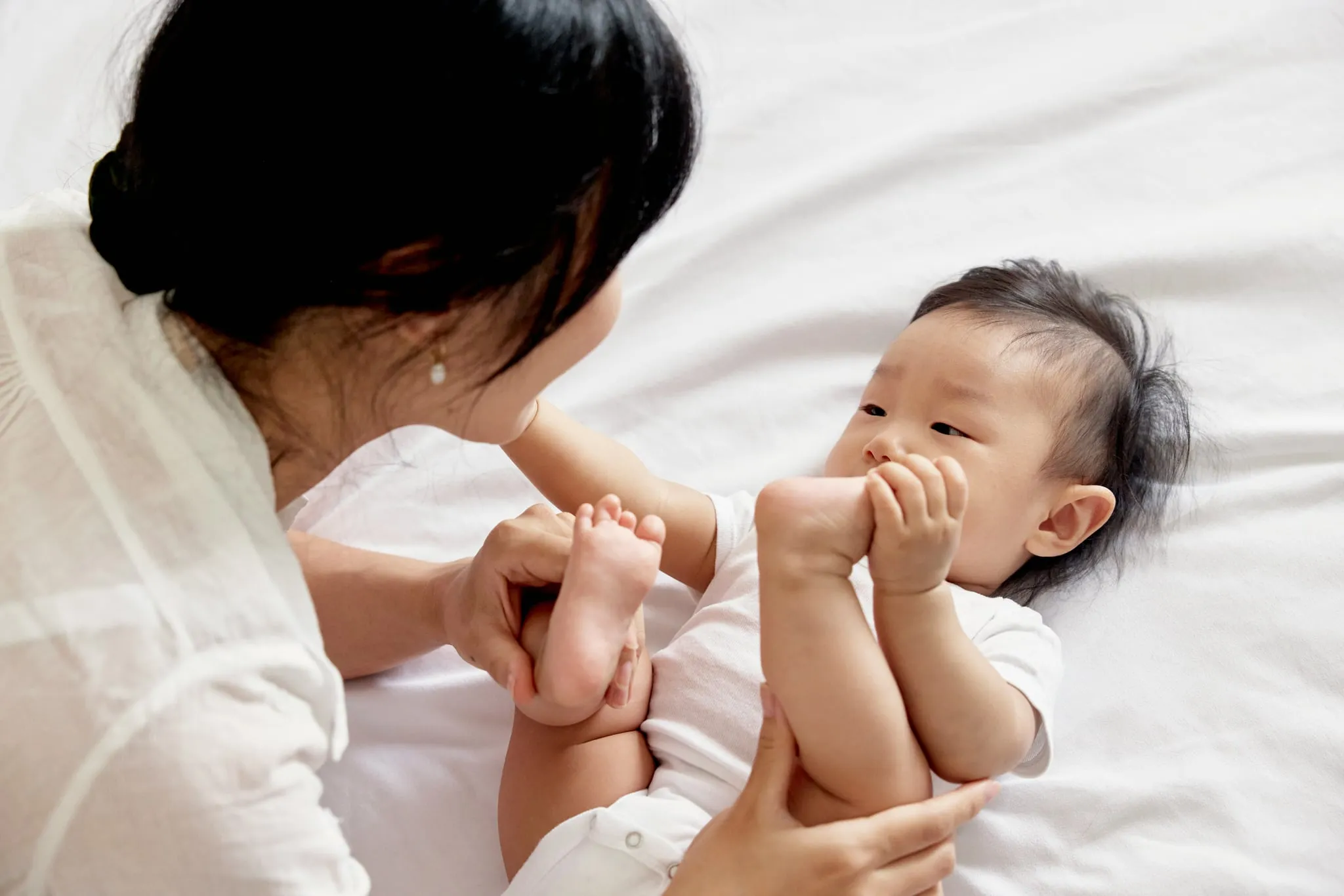 A parent playing with their baby on a bed